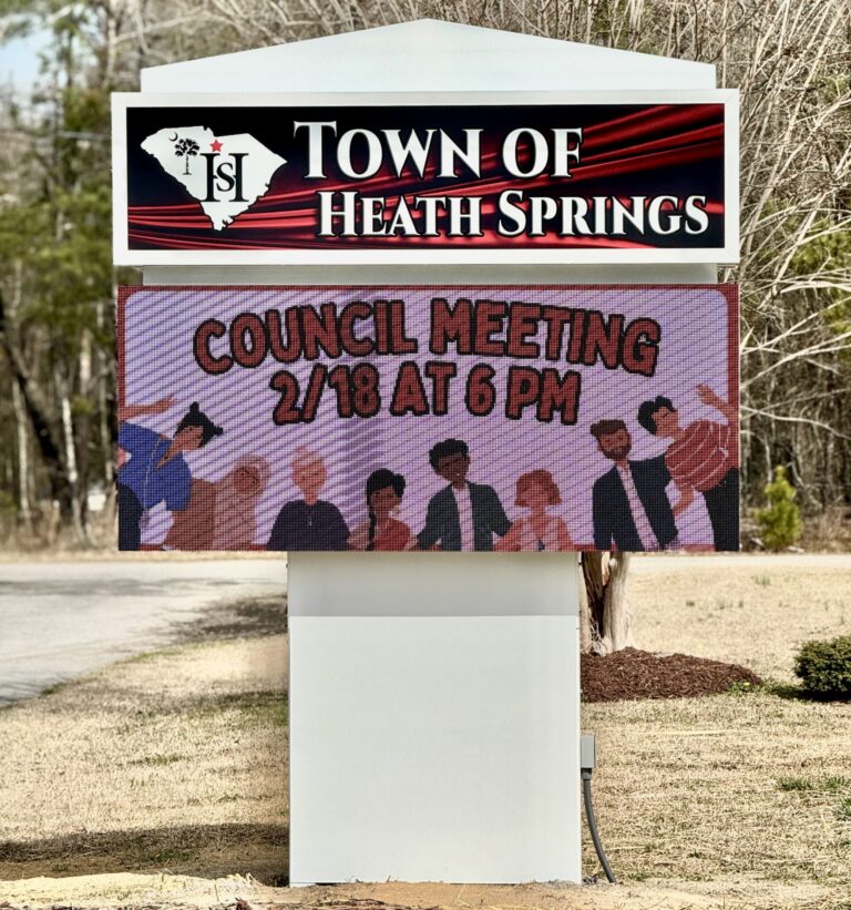 Digital sign in Heath Springs announcing a council meeting on 2/18 at 6 PM, with illustrated people below text.