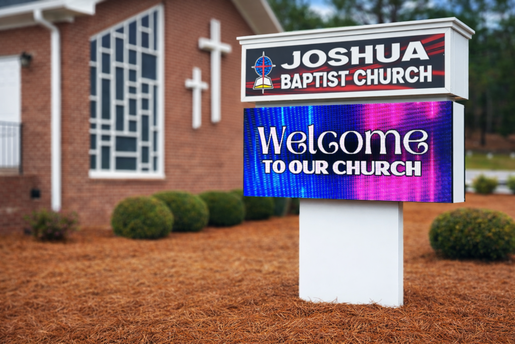 A sign outside Joshua Baptist Church reads Welcome to our church near a brick building with crosses.